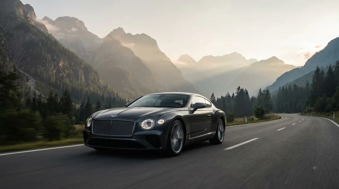 Une voiture de prestige parcourant une route de montagne sinueuse dans la brume du matin.