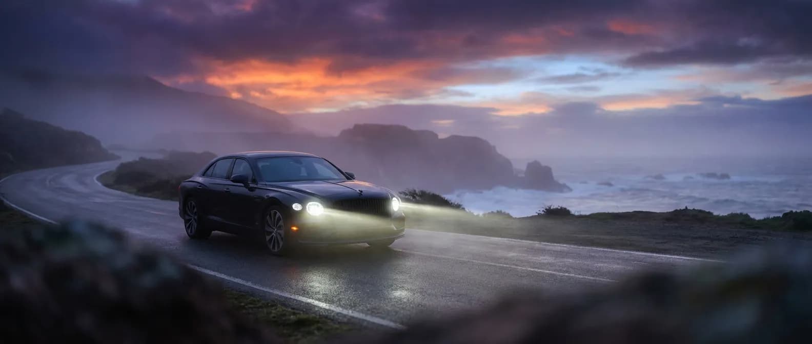 Une voiture de luxe garée sur une route côtière au crépuscule, illustrant la puissance et la fiabilité du démarrage