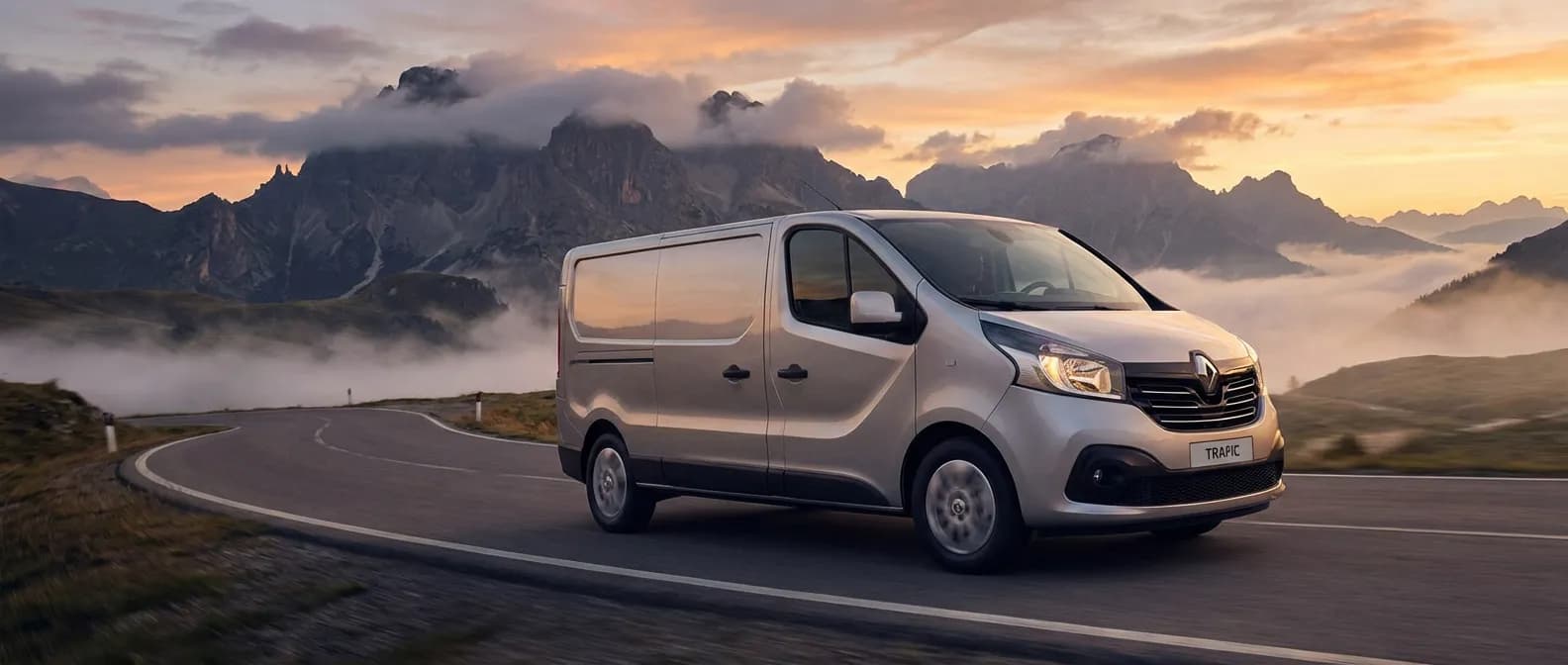 Renault Trafic 2.0 dCi 115 circulant sur une route de montagne majestueuse au lever du soleil.